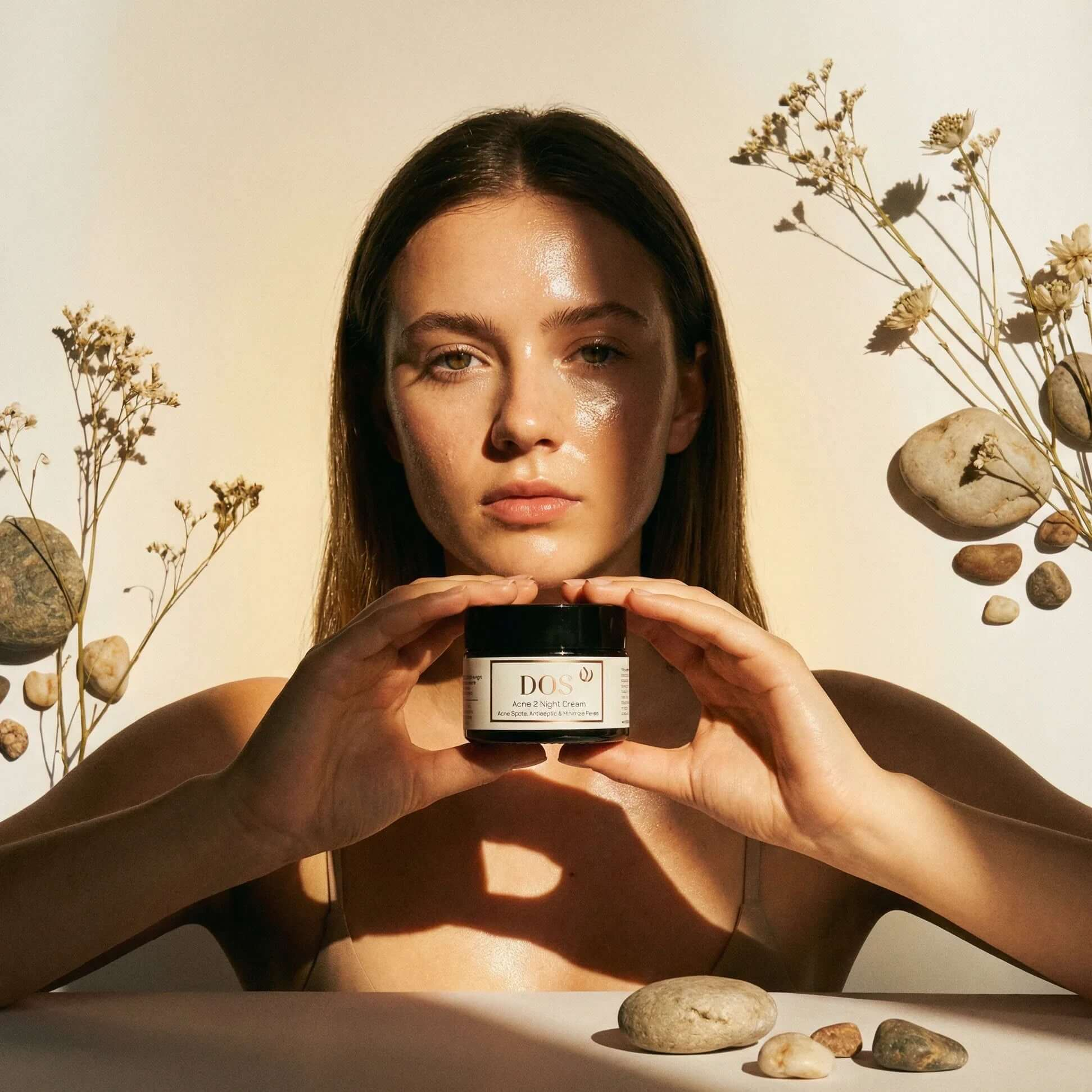 Acne night cream for acne-prone skin held by model surrounded by stones and flowers in natural light. DOS Cosmetics