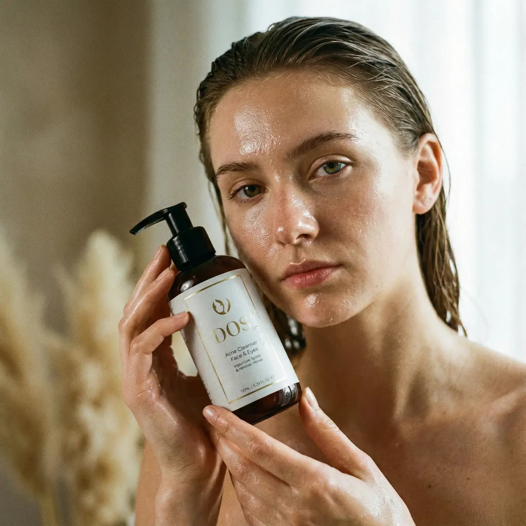 Woman holding Acne cleanser bottles from DOS Cosmetics skincare product with a blurred background