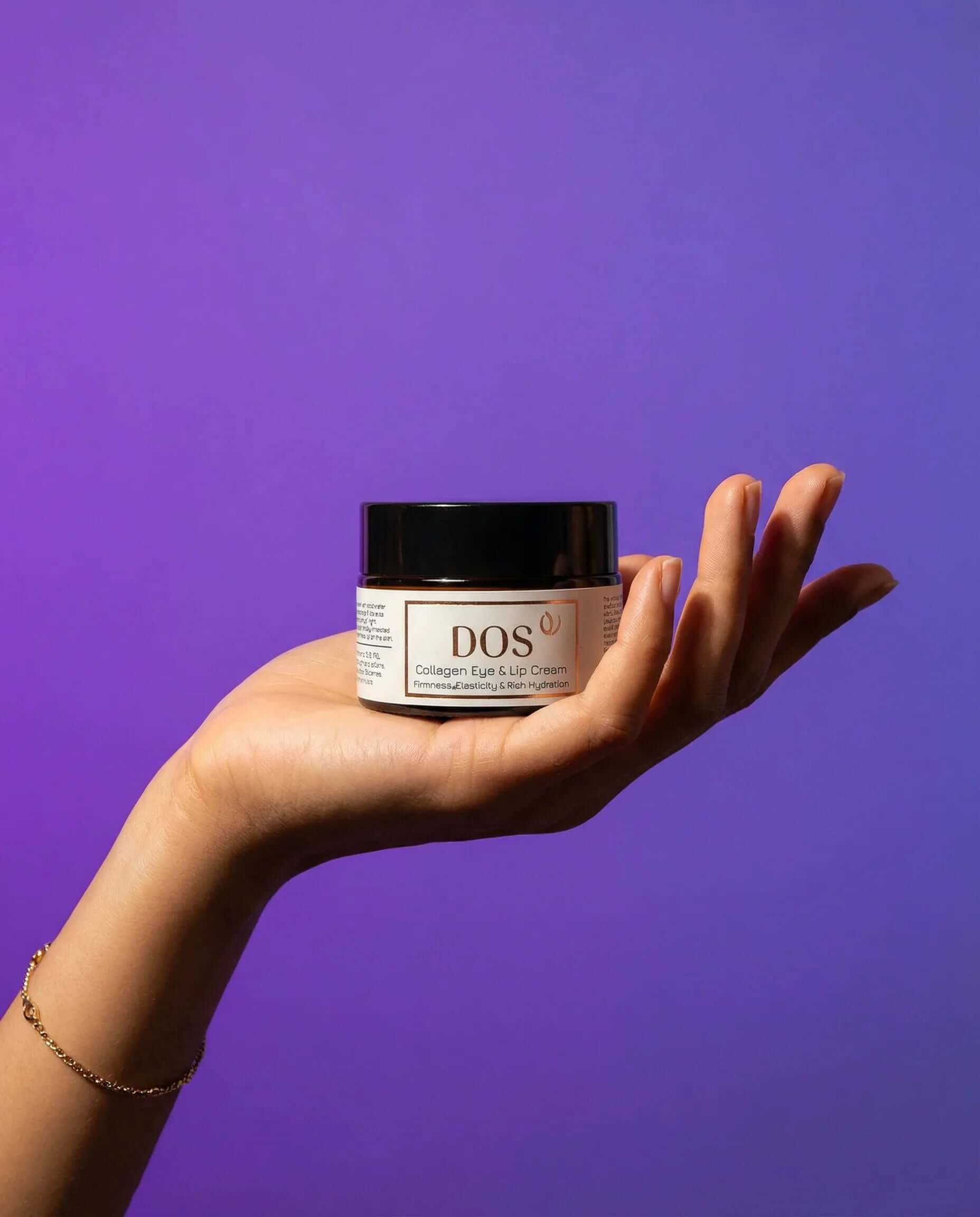 Hand holding a jar of Collagen Eye Cream against a purple background for revitalizing care. DOS Cosmetics