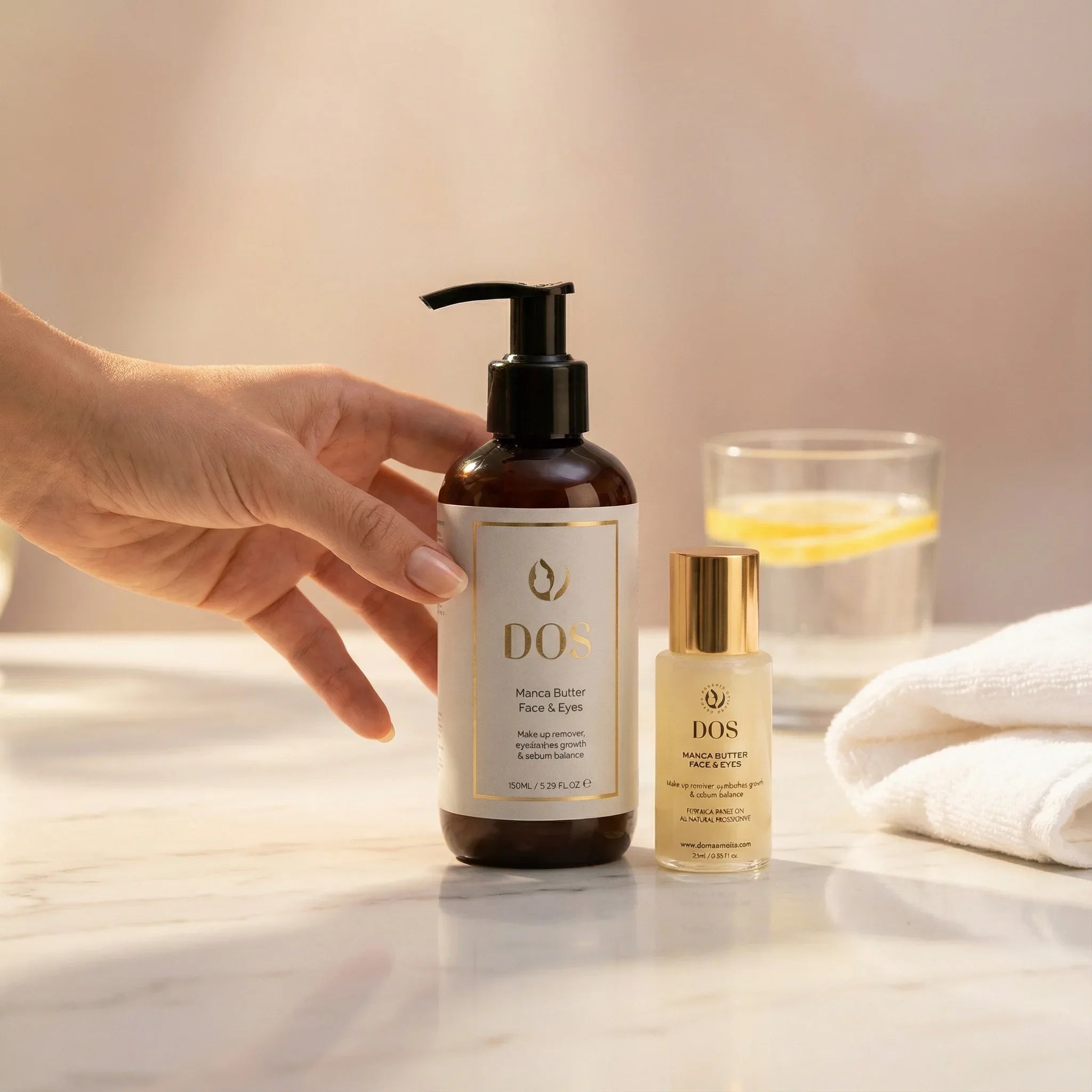 Hand holding Manca butter of DOS skincare product on a reflective surface with a glass and towel in the background in two sizes