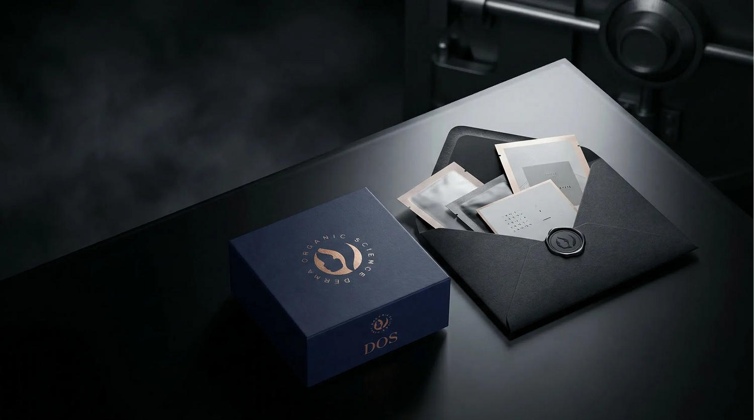 Caja azul de DOS Cosmetics con un sobre negro sobre una superficie oscura, con la marca.
