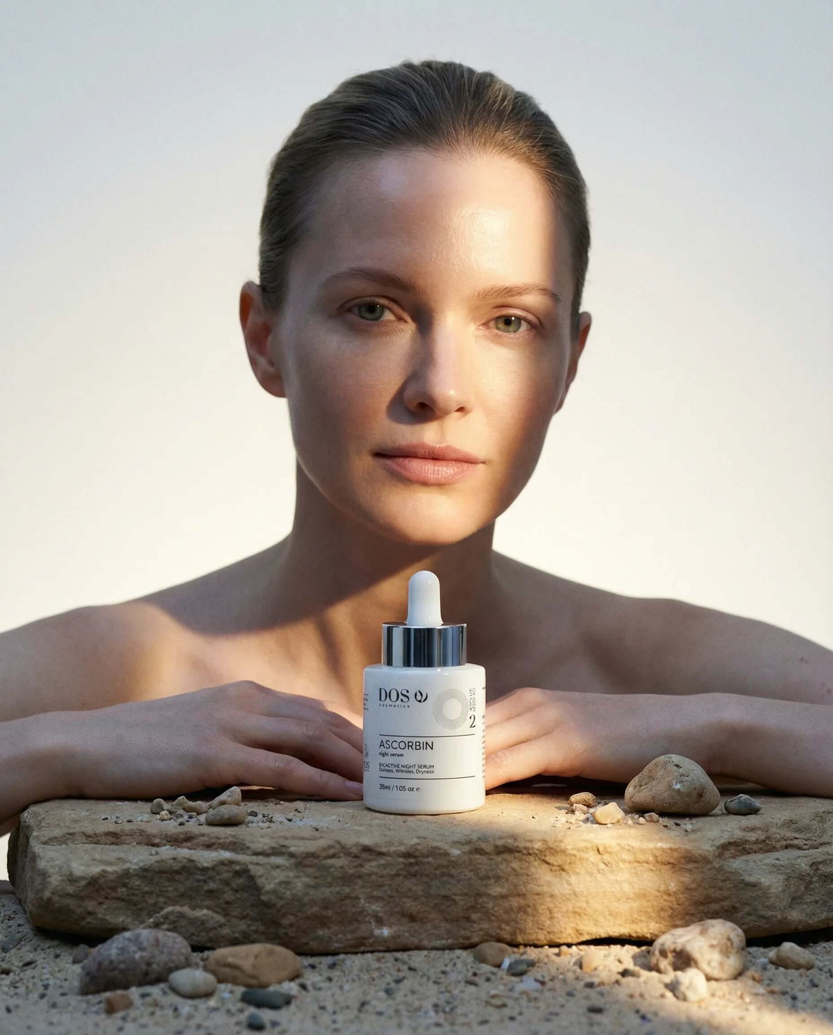 Vitamin C serum Ascorbin displayed in front of a woman with radiant skin on a natural stone background. DOS Cosmetics