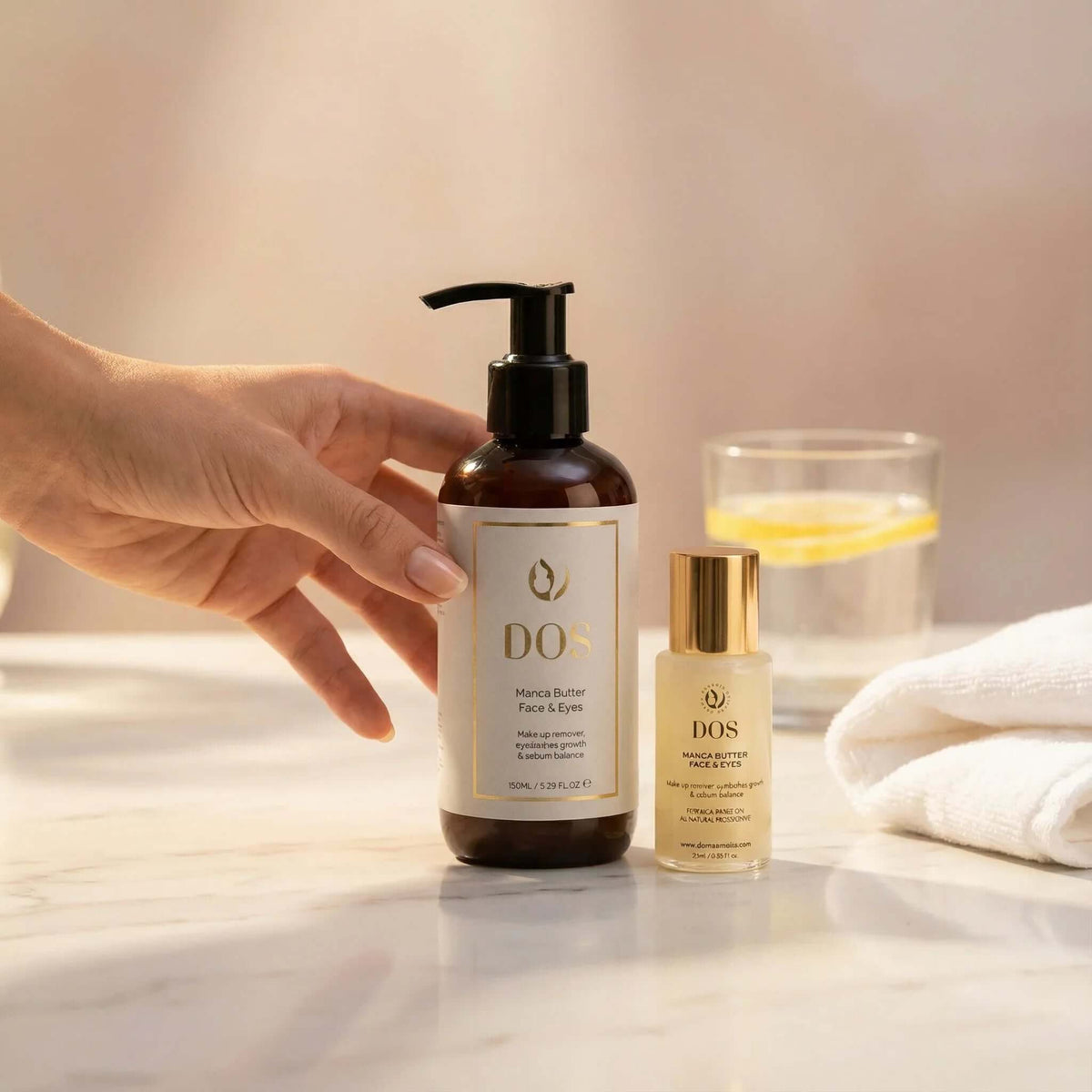 Makeup remover Manca Butter Face &amp; Eyes bottle held by a hand next to another skincare product on a marble surface. DOS Cosmetics