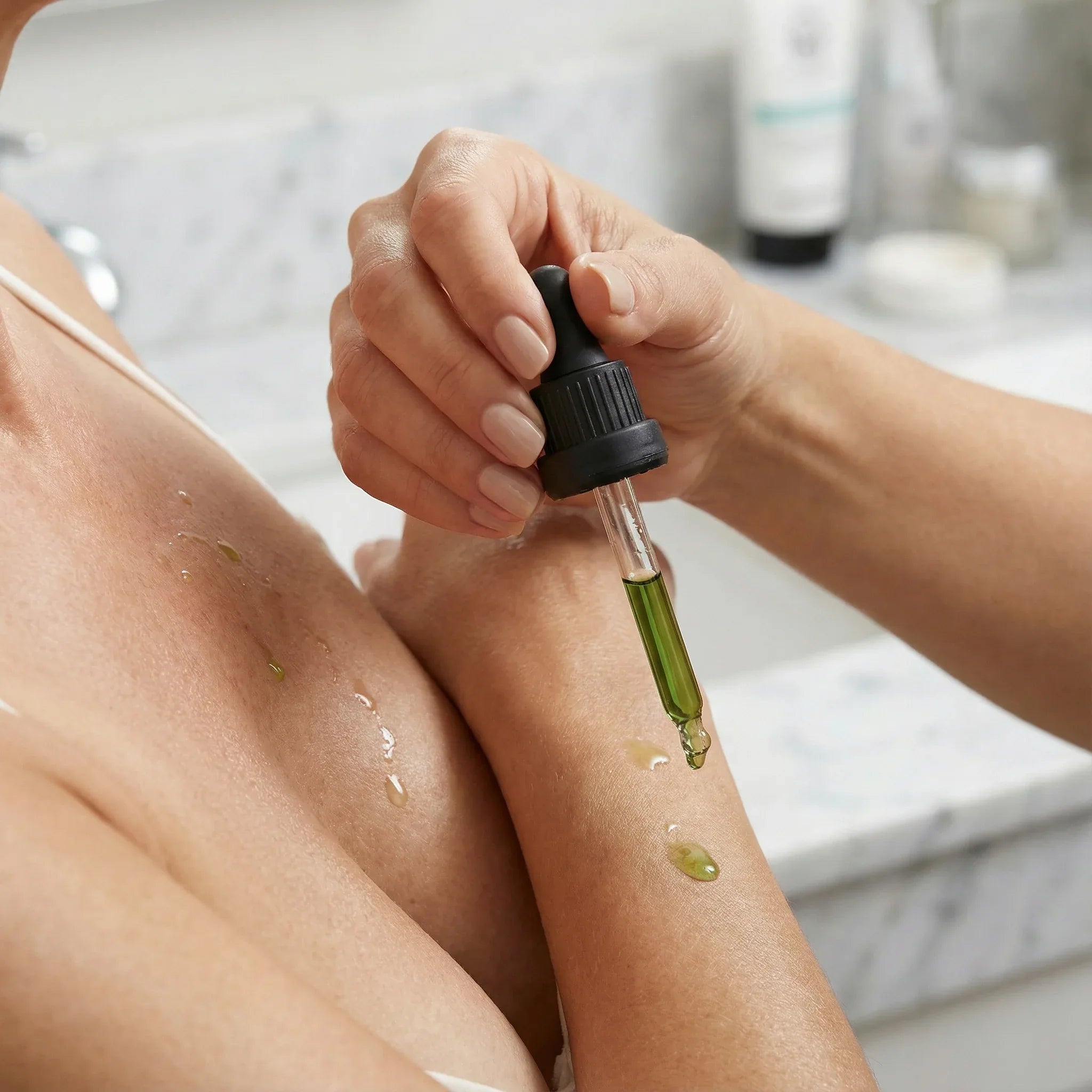 Woman applying green avocado oil from a dropper to her skin in a bathroom setting - DOS Cosmetics
